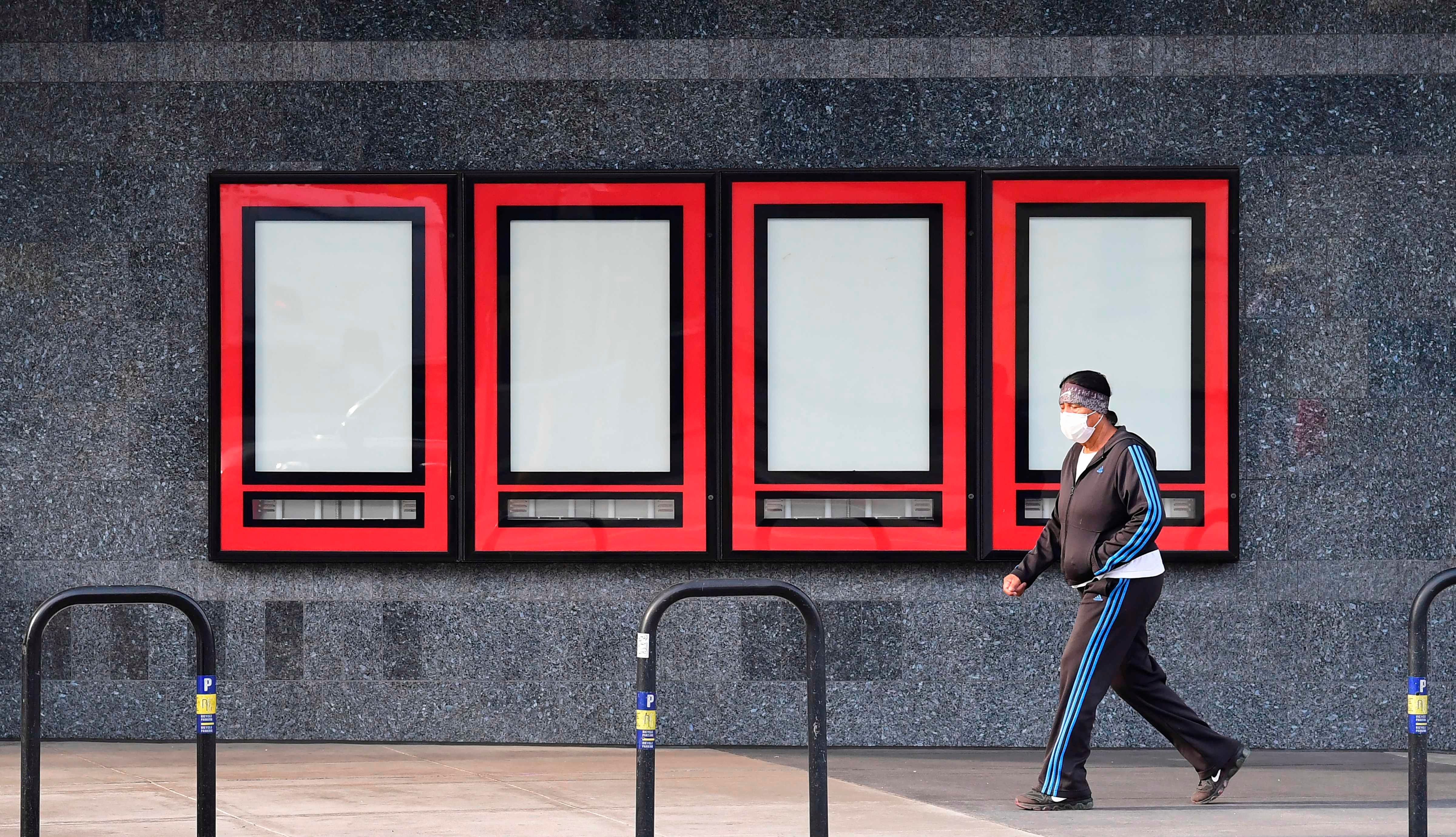 A pedestrian in a facemask walks past empty cases where upcoming movies were once displayed at Regal Cinemas on Oct. 5, 2020 in Los Angeles. The second-largest operator of theaters in the U.S., Regal plans to close 500 theaters, affecting some 40,000 employees, due to the coronavirus pandemic.