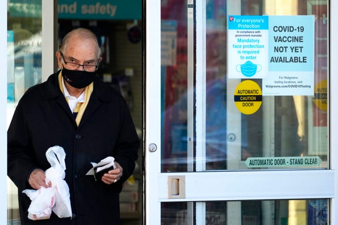 A customer wears a mask as he walks out of a Walgreen's pharmacy store and past a sign advising that a COVID-19 vaccine is not yet available at Walgreens in Northbrook, Ill., Thursday, Dec. 4, 2020. (AP Photo/Nam Y. Huh)