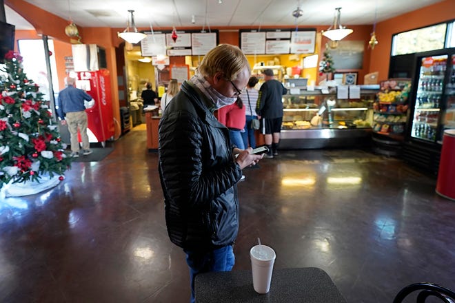 Blake Opseth looks over his smart phone while waiting for his lunch order at at the San Francisco Deli in Redding, Calif., Thursday, Dec. 3, 2020. Brenda Luntey, who owns the deli with her husband, is openly violating the state's order to close her restaurant to indoor dining. Luntey wants her customers and critics to know she is not a rule-breaker, and that it's a matter of survival. (AP Photo/Rich Pedroncelli)