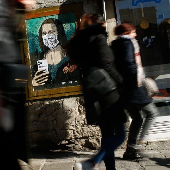 People walk past a poster by Italian urban artist Salvatore Benintende, aka "TVBOY," depicting Leonardo da Vinci's Mona Lisa  wearing a protective face mask and holding a mobile phone reading "Mobile World Virus" in Barcelona, Spain, on February 18, 2020.