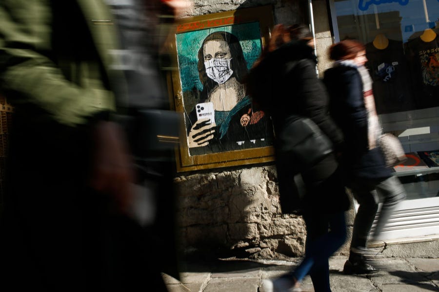 People walk past a poster by Italian urban artist Salvatore Benintende, aka "TVBOY," depicting Leonardo da Vinci's Mona Lisa  wearing a protective face mask and holding a mobile phone reading "Mobile World Virus" in Barcelona, Spain, on February 18, 2020.