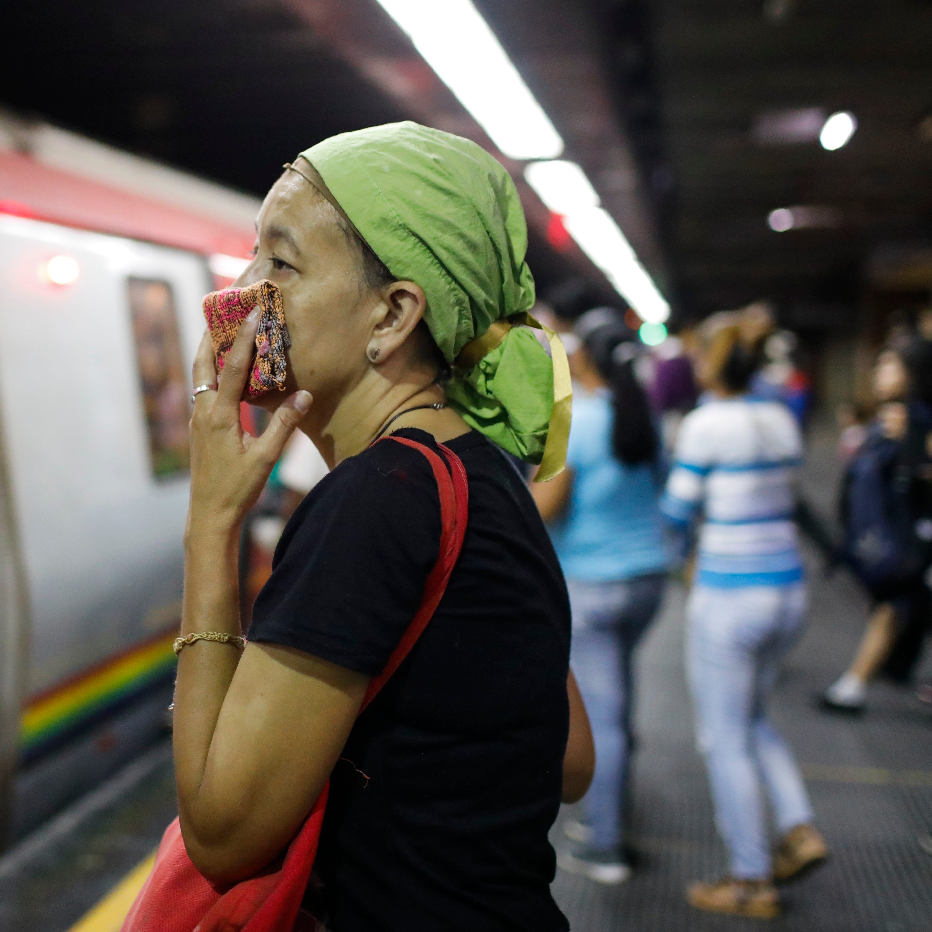 A woman covers her mouth and nose with a wash cloth on a subway platform in Caracas, Venezuela, Friday, March 13, 2020. Venezuela's Vice President Delcy Rodr’guez confirmed Friday the first two cases of the new coronavirus in the South American country. The vast majority of people recover from the new virus. 