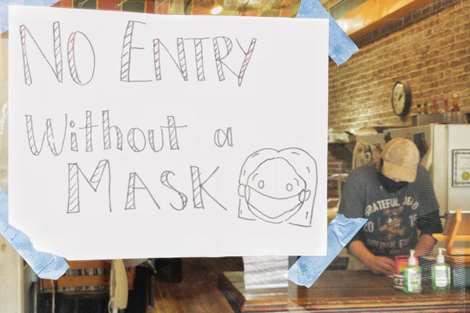 Employee Jacob Ettinger works at the front counter just beyond a sign on the front door that instructs diners they must wear a mask to enter the building at Baked Pizza, 57 S. Seminary St. on Dec. 9, 2020.