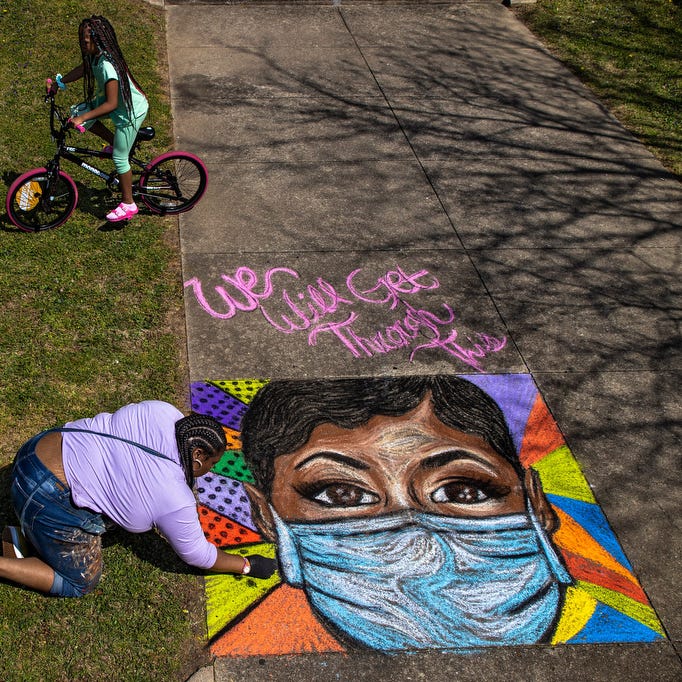 Makenzi Elliott, from left, and twin sister Madison Elliott, ride their bikes past as Louisville artist and West End Boys School teacher, Jaylin Stewart, finishes a chalk art portrait of a healthcare worker outside her apartment building along 42nd Street in Louisville on April 4, 2020. 