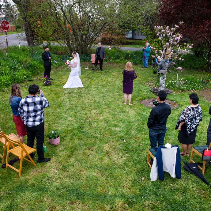 Bride Nova Connolly, center left, joins groom Edwin Nunez, left, for a socially distant wedding ceremony in her parents yard in Eugene, Ore, on Friday April 3, 2020. The couple originally planned to be married May 23rd, but decided to a hold a smaller wedding now because of COVID-19. 