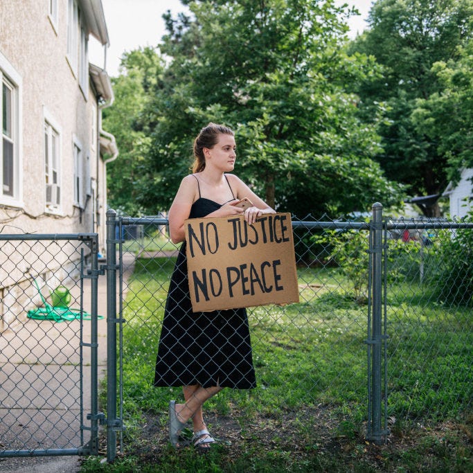 A woman holds a sign while looking on as a demonstration passes her front yard on June 25, 2020 in Minneapolis, Minnesota. 