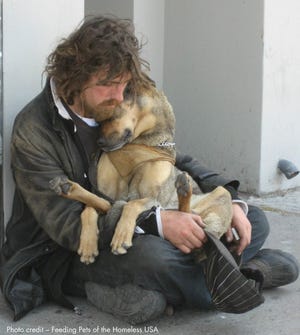 A homeless man holds his dog as he sits on the pavement. One of the past recipients of an A Community Thrives grant was Feeding Pets of the Homeless.