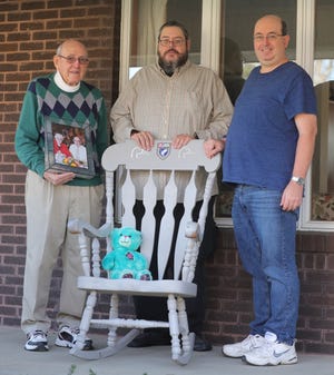 Dick Reymann holds a photo of himself and his late wife Mary Ellen as he stands with sons Keith, center, and Jeff on  Dec. 11 in Akron.