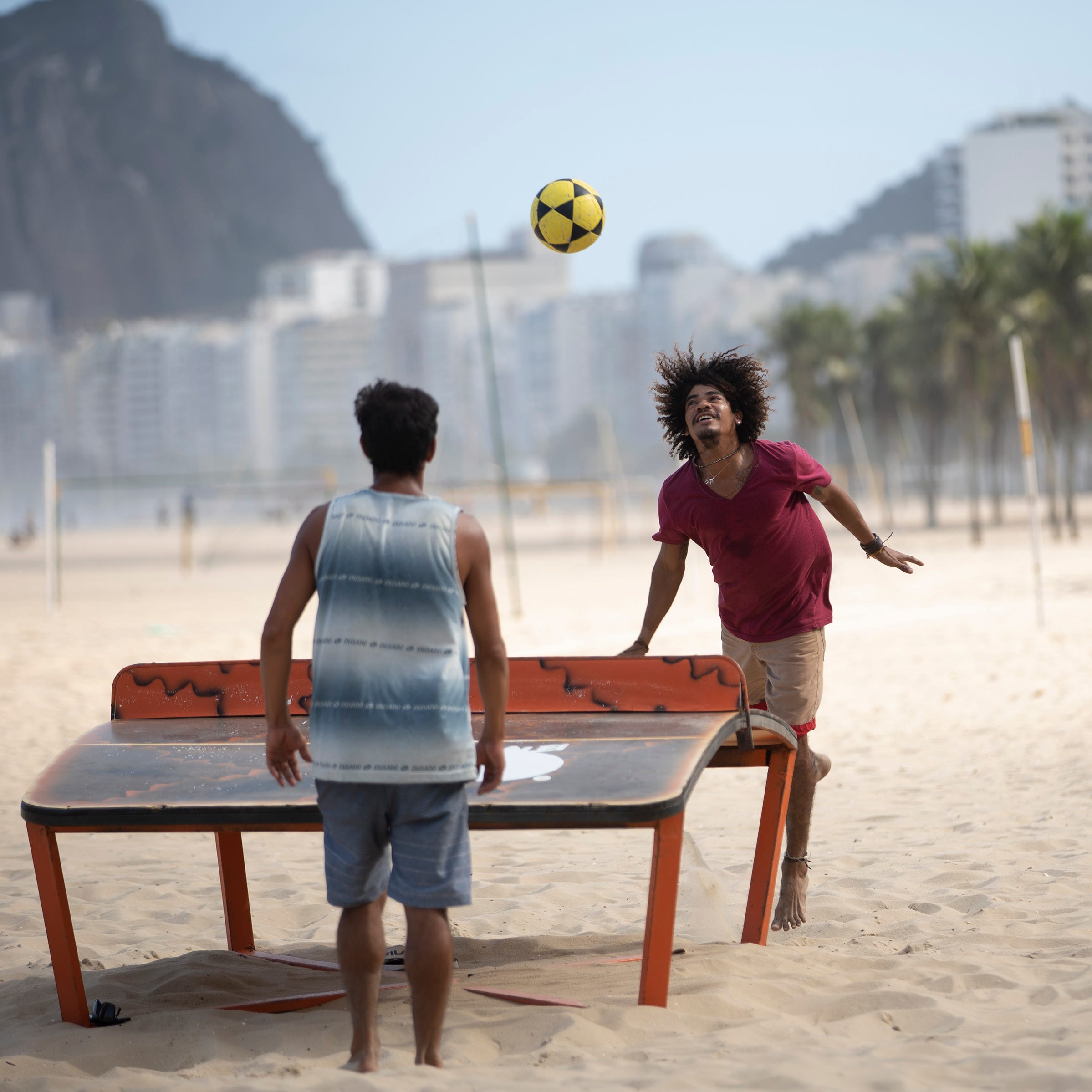 Two men play teqball amid the new coronavirus pandemic on Copacabana beach in Rio de Janeiro, Brazil, Thursday, July 2, 2020, as authorities begin to ease the city's lockdown against the growing COVID-19 pandemic. Teqball is played over a curved table combining elements of soccer and table tennis. 