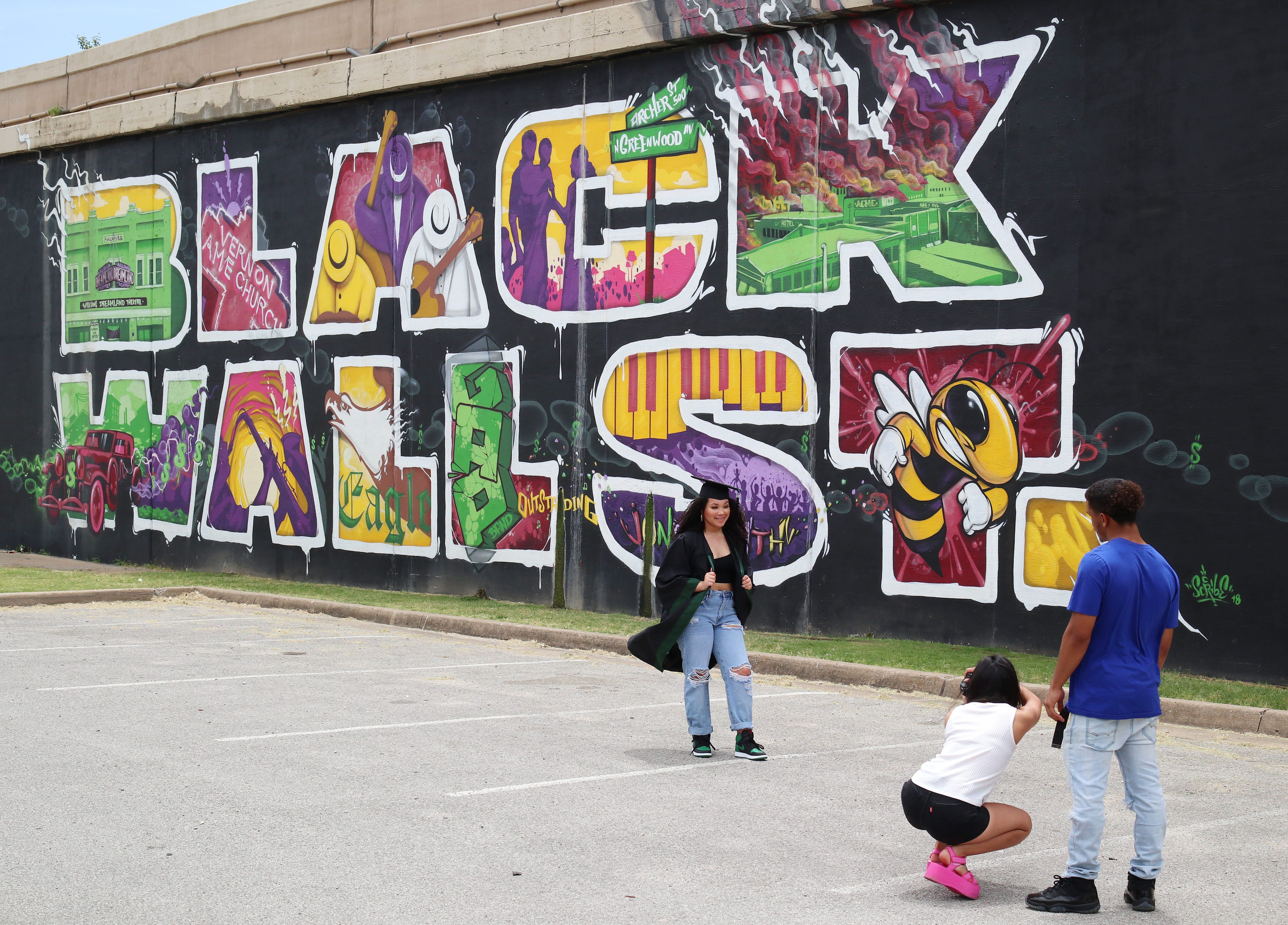 Muskogee High School graduate Amitie Esparaza has her photo taken by Fatima Ledezma as Ty Davis assists in front of the Black Wall Street mural on the north side of I-244 highway that runs through the historic Greenwood District in North Tulsa, know at the time as the Black Wall Street, the site of a massacre of African Americans by a white mob, resulting in hundreds of deaths in 1921, in Tulsa Friday, June 12, 2020.