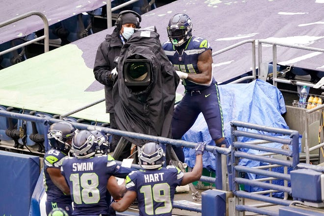 Seattle Seahawks wide receiver DK Metcalf (14) briefly takes over a broadcast camera to point at his teammates after climbing into the stands after he scored a touchdown against the New York Jets during the first half of an NFL football game, Sunday, Dec. 13, 2020, in Seattle. (AP Photo/Ted S. Warren)