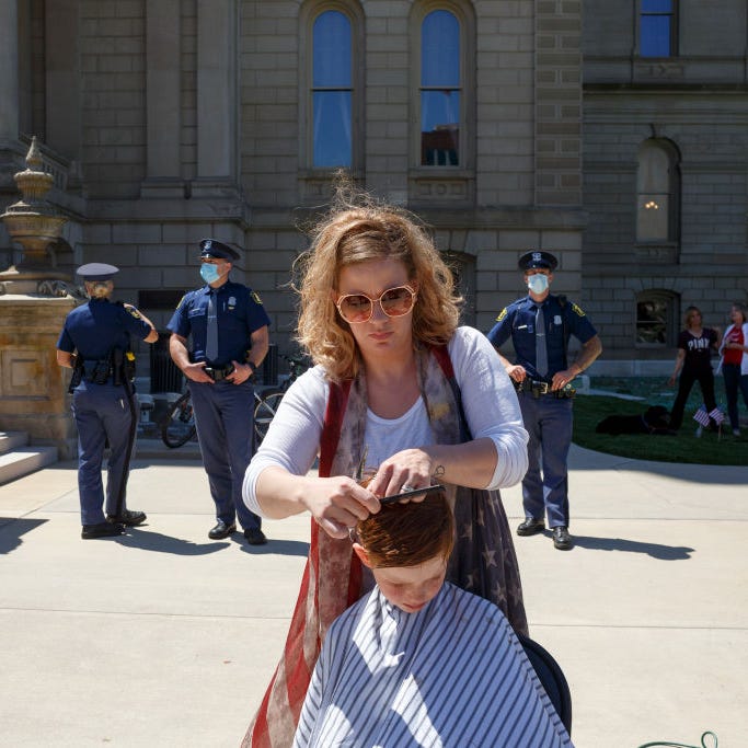 Danielle Ashcraft gives a free haircut to a child near the steps of the state Capitol during Operation Haircut on May 20, 2020 in Lansing, Michigan. The event was a protest planned by the Michigan Conservative Coalition in response to an Owosso barber, Karl Manke, whose business license was taken away after he violated the stay-at-home order by reopening.