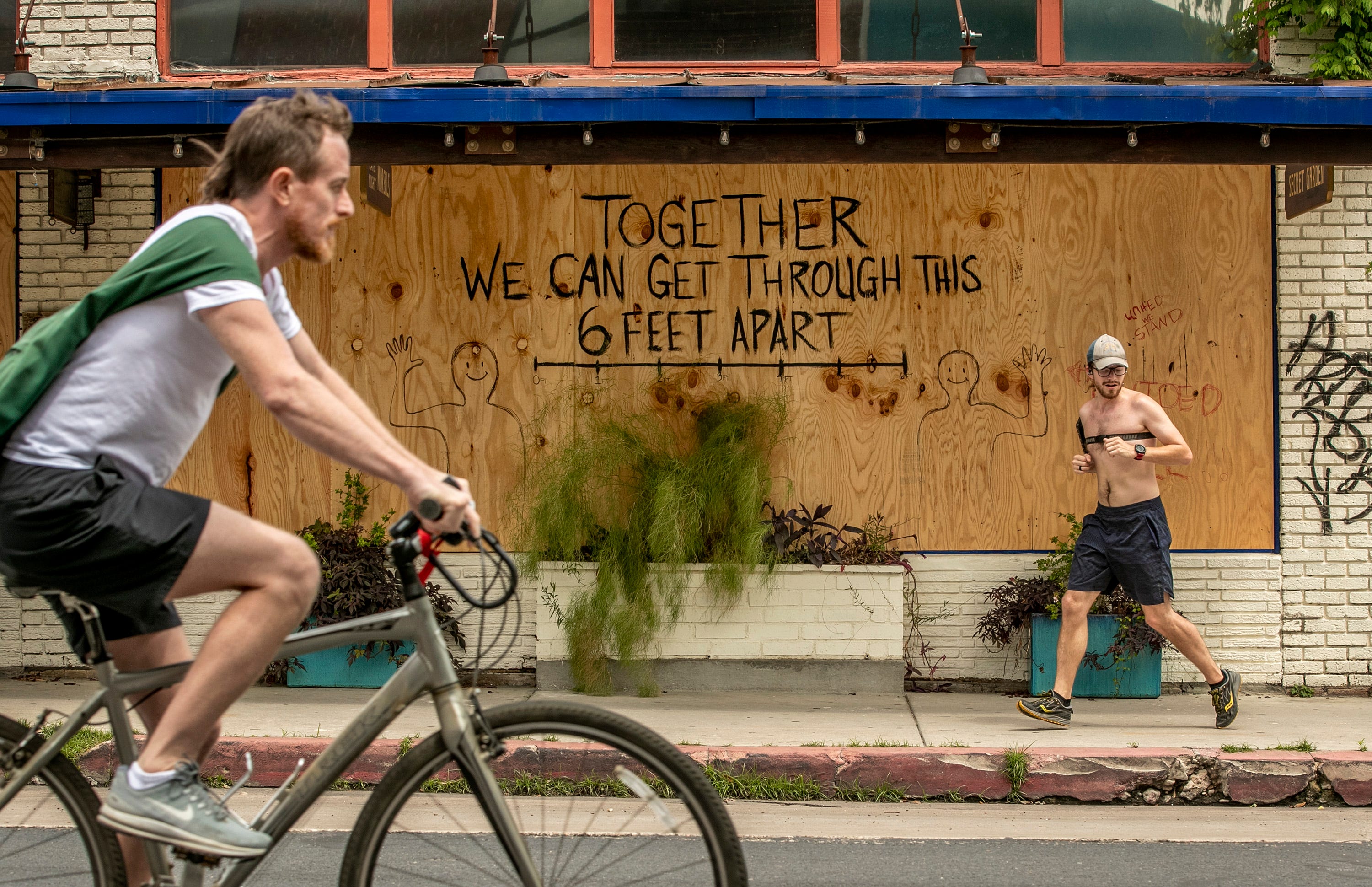 Jorden Stanley, right, runs past a hopeful message on a boarded up bar on East 6th Street on Monday April 6, 2020, during a shelter in place order due to the coronavirus pandemic.