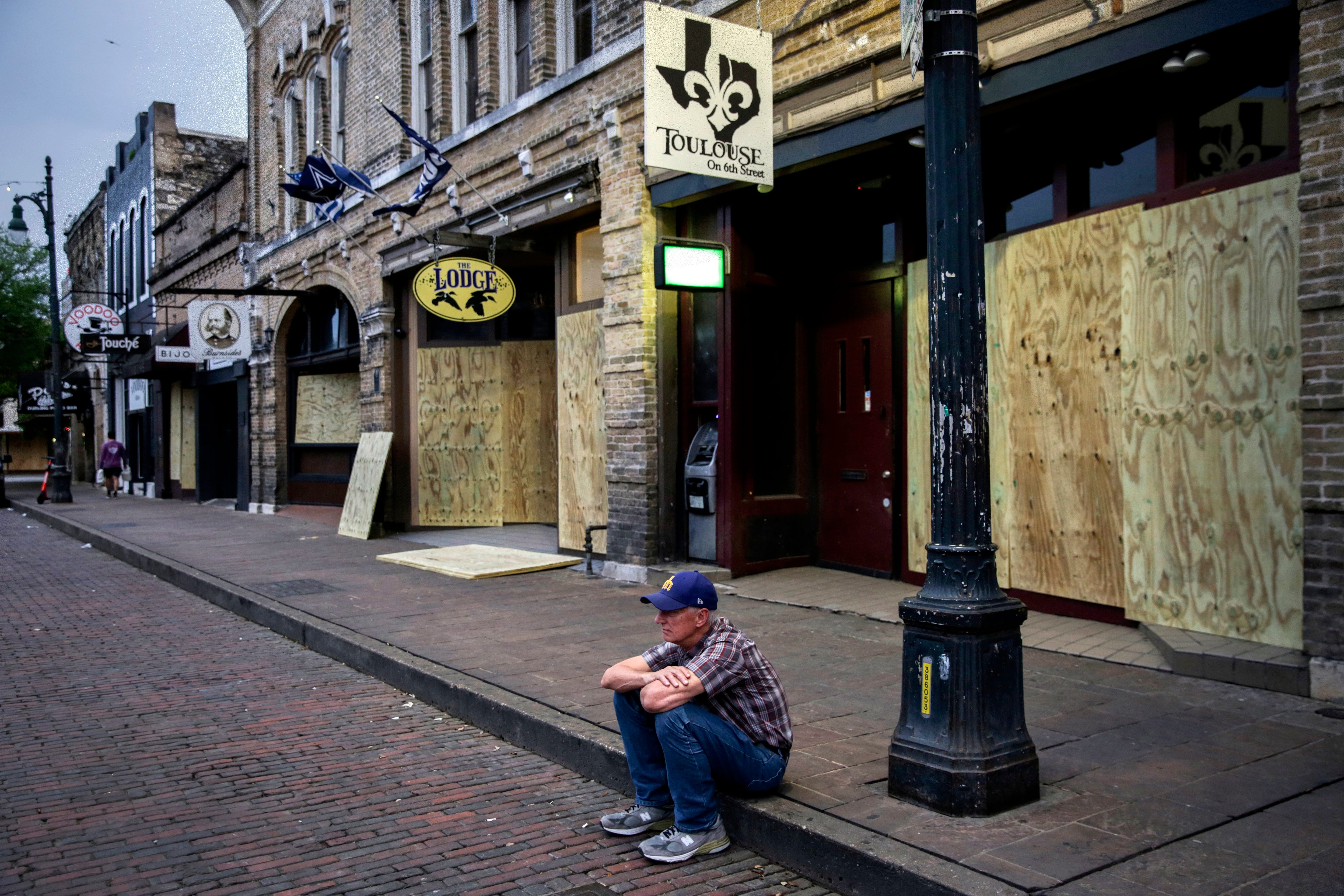 Chris Jones, 65, sits on the curb in front of several bars that are boarded up on East 6th Street in Austin on Wednesday, March 18, 2020. This comes after Austin officials ordered closures of all bars and restaurants. "I see lost money," Jones said. "Those people have families and they are not going to get money to support themselves for six weeks."