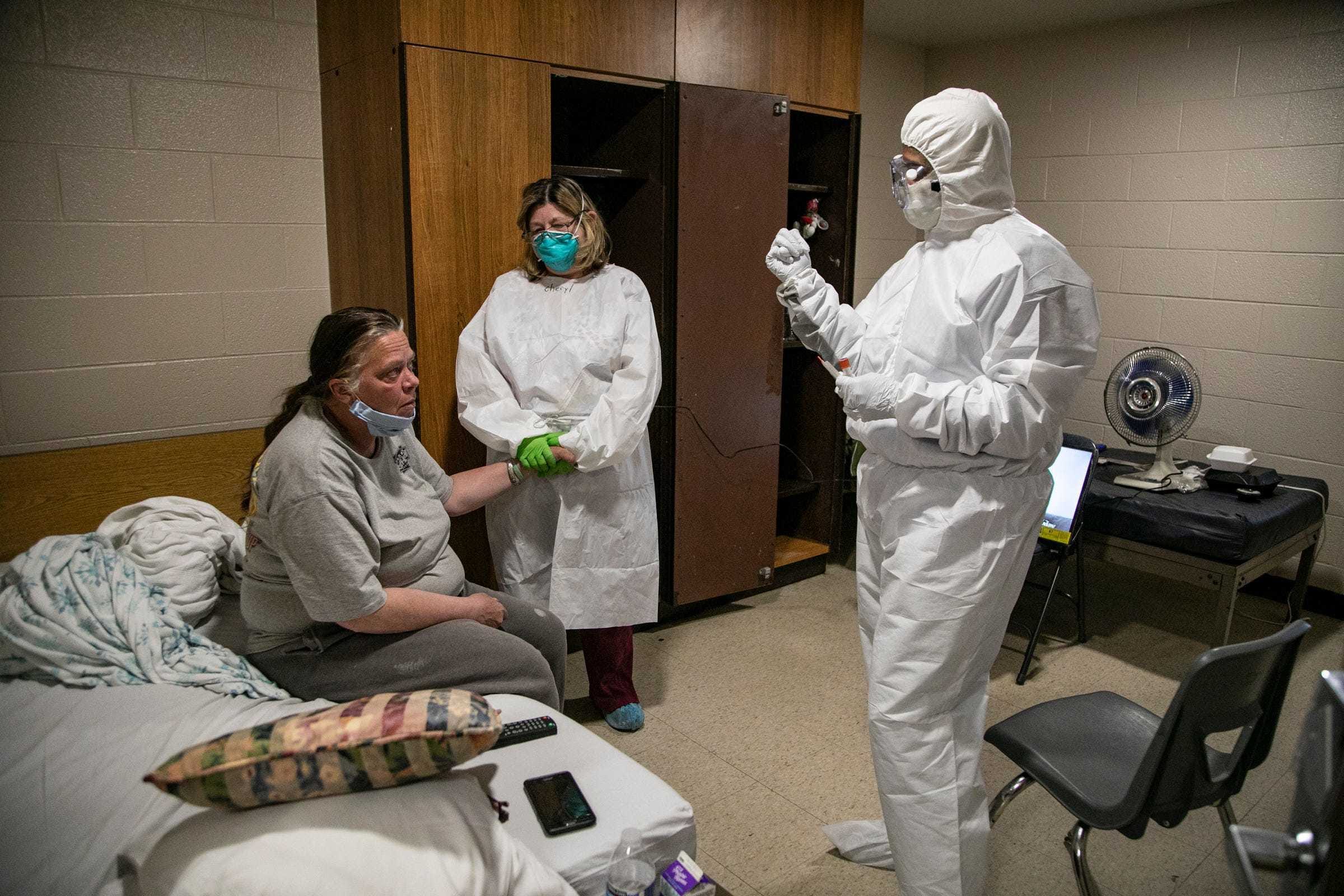 Marsha Roderick, 50, left, has her hand held by case manager Cheryl Linari before Dr. Neeli Thati administers a nasal swab to test for COVID-19 Friday, May 8, 2020 in her room at Salvation Army Harbor Light in Detroit. Salvation Army Harbor Light in Detroit has set up wings in its facility to take on testing and some treatment of COVID-19 positive and pending.