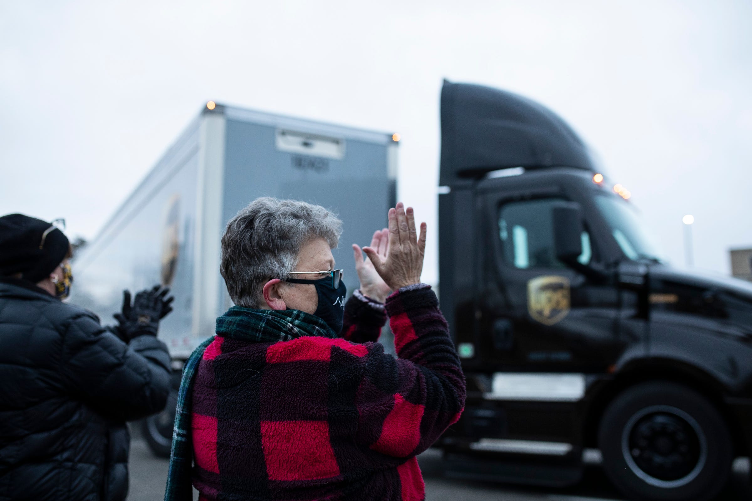 Susan Deur of Plainwell, center, and Nancy Galloway of Plainwell, left, applaud and cheer as they watch the trucks carrying COVID-19 vaccine leave at Pfizer Global Supply in Portage, Mich., Sunday, Dec. 13, 2020.