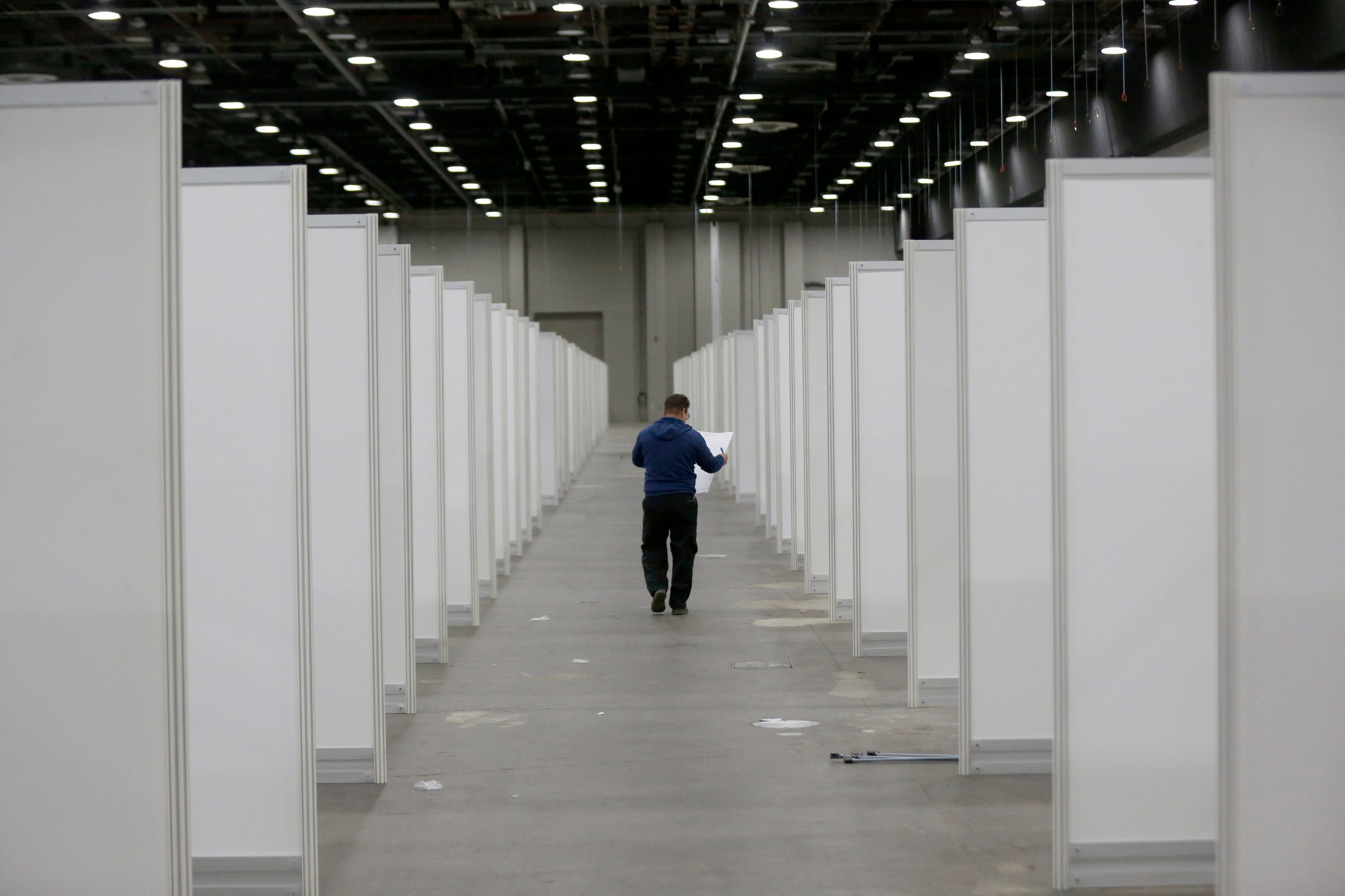 A worker inside Hall C looks over plans as he heads down the aisle with individual rooms on both sides of him at the TCF Center in Detroit, Michigan on Wednesday, April 1, 2020. One thousand rooms with beds were being assembled for the alternate care facility at the convention center in downtown Detroit.

