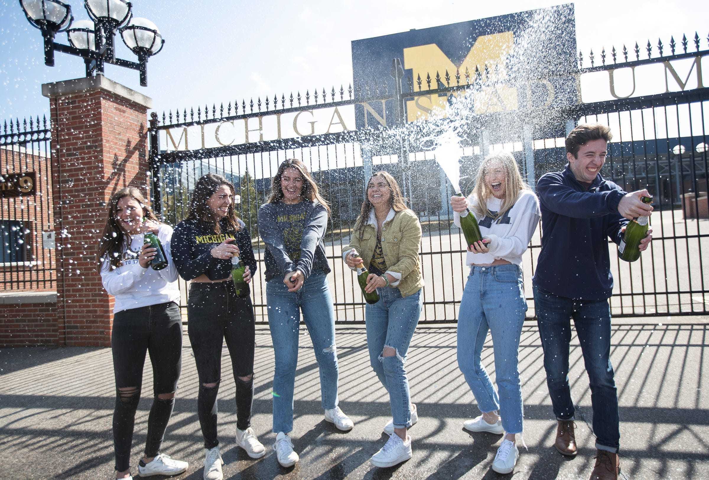 From left, University of Michigan graduating seniors Grace Scarfone, Natalia Engel, Rita Sidhu, Hannah Saunders, Grace Drettmann and Brian Galvin pop bottles of sparkling wine for their graduation photos outside of the Michigan Stadium in Ann Arbor, Tuesday, March 17, 2020. Students weren't given their traditional graduation due to the pandemic.