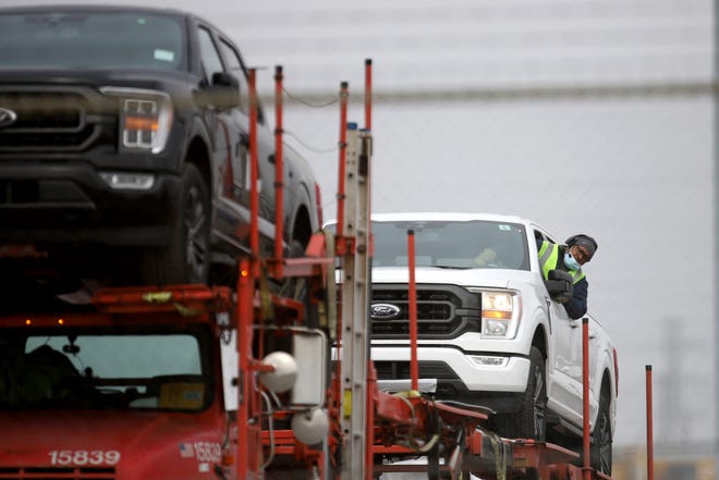An unidentified worker loads a Ford F-150 onto a car carrier trailer in the parking lot of TDM, Troy Design and Manufacturing Co., on Monday, Dec. 21, 2020, in Flat Rock.