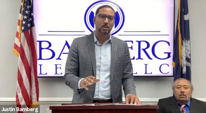 In this screengrab from video provided by Bamberg Law, LLC, attorney Justin Bamberg, standing, speaks at a news conference as plaintiff Jethro DeVane, seated at right, listens Tuesday in Orangeburg, S.C.