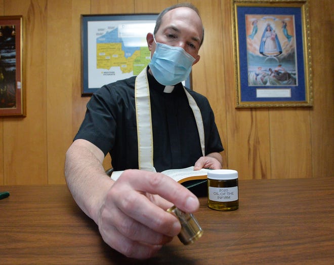 The Rev. Chris Singer, chancellor for the Catholic Diocese of Erie and anointer of many sick COVID-19 patients, displays a small container of anointing oil and a prayer book he regularly uses with patients.