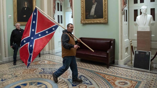 A Pro-Trump rioter carries a Confederate flag near