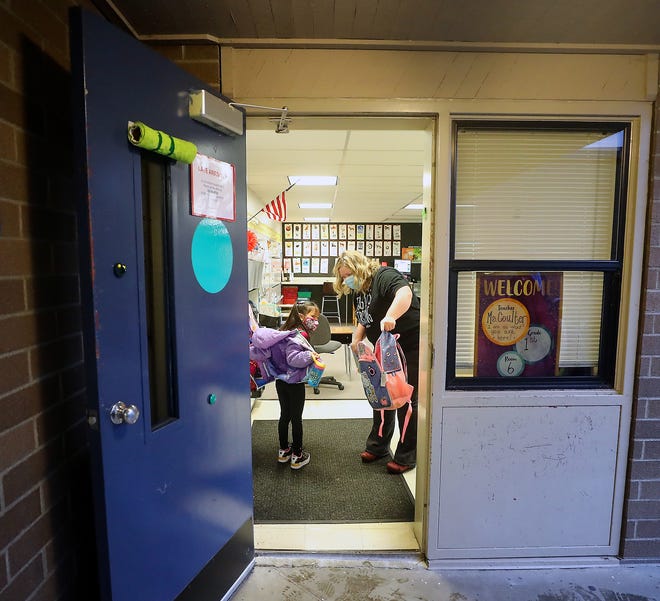 FILE — First-grade teacher Amee Coulter helps a student take off her backpack and coat inside the classroom at Esquire Hills Elementary School in January 2021.