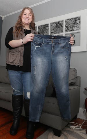 Riley Ickes, 16, a student at Ellet High School holds up an old pair to pants in the living room of her family’s home on Monday Jan. 10, 2021 in Akron. Ickes has lost more than 90 pounds since having gastric sleeve surgery in September at Akron Children’s Hospital. She has changed her lifestyle -working out 4 to 5 times a week and watching her diet.   [Mike Cardew/Beacon Journal]