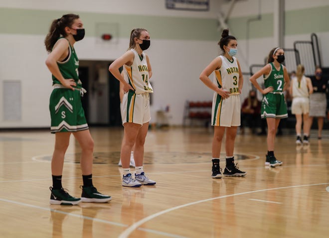 Players from Notre Dame Academy and Sutton stand by in between plays sporting masks per MIAA guidelines during a game last season.