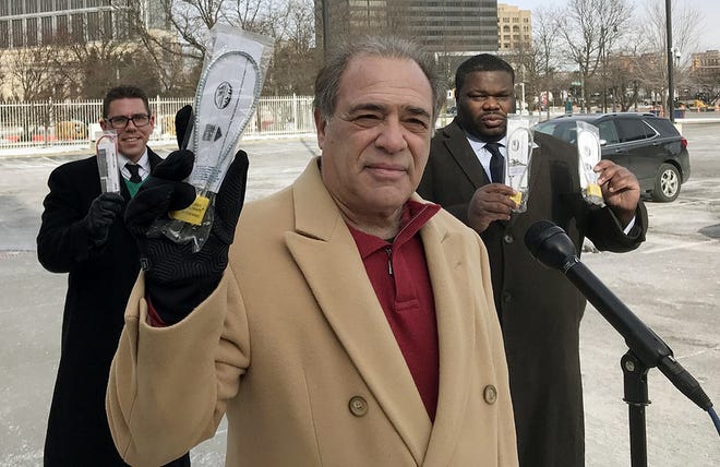 Former Wayne County Sheriff Robert Ficano holds up a gun lock, offered free at Detroit police precinct offices and at police departments across metro Detroit. He is standing outside Detroit police headquarters on Jan. 30, 2021. Behind him, from left: activist Tom Choske and Detroit Police commissioner Willie Burton.