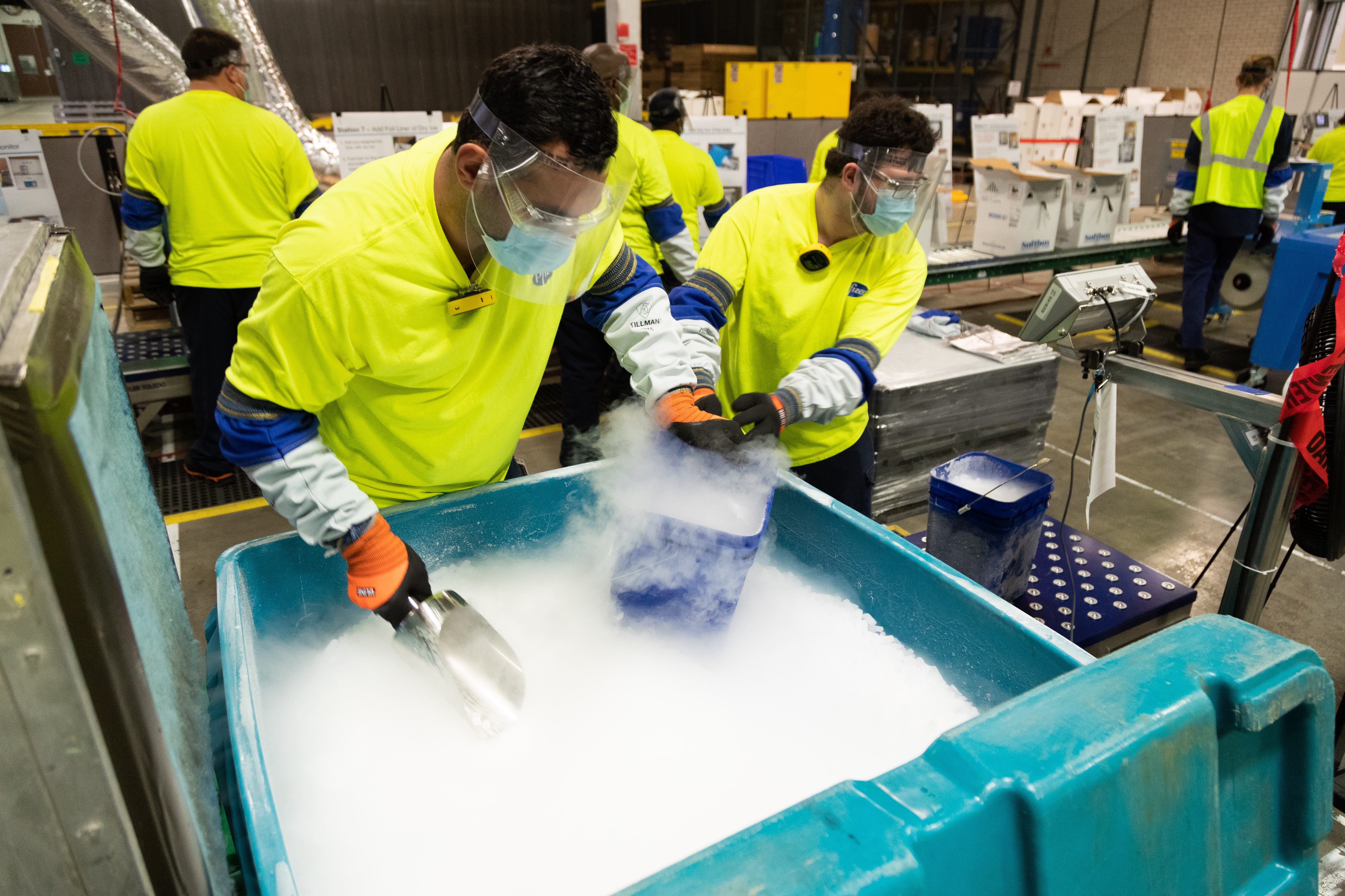 Workers at Pfizer's manufacturing site in Kalamazoo, Michigan, fill buckets with dry ice that will be poured into thermal shipping containers holding the COVID-19 vaccine. The thermal shippers are used to ship vaccines from Pfizer plants to their intended destinations at the required subzero temperature.