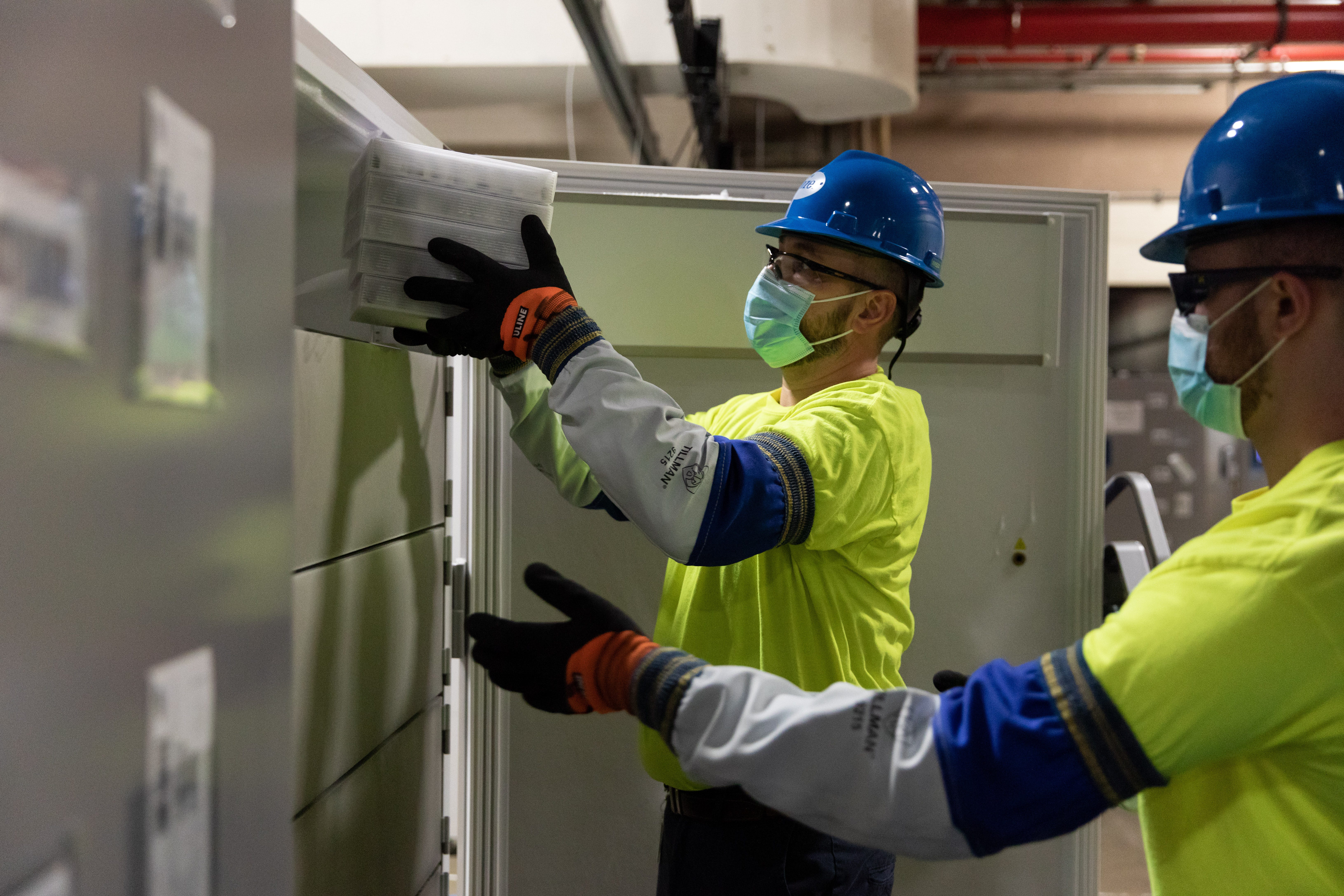 Workers remove COVID-19 vaccine kept in ultracold refrigerators at Pfizer's manufacturing site in Kalamazoo.