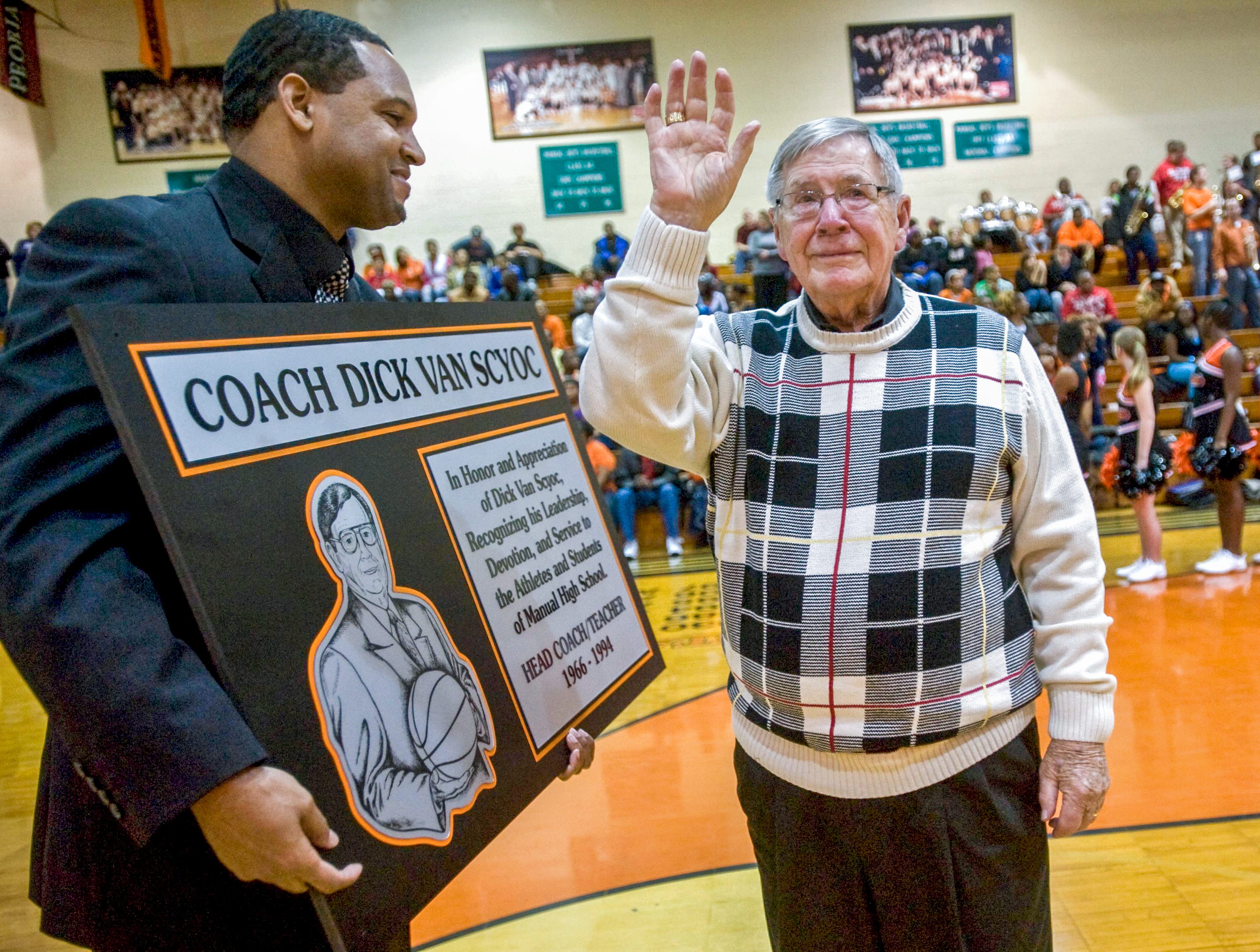 Former Manual High School basketball coach Dick Van Scyoc waves to the crowd as Derrick Booth presents him with a plaque for his years of service as a coach and teacher at the school from 1966-1994 at a ceremony Dec. 18, 2009 in the Manual High School gym.