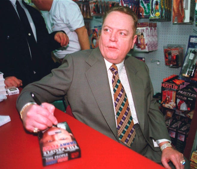 FILE - "Hustler" Magazine publisher Larry Flynt signs a copy of "The People Vs. Larry Flynt" in his downtown Cincinnati "Hustler" store on April 30, 1998. Flynt, who turned "Hustler" magazine into an adult entertainment empire while championing First Amendment rights, has died at age 78. His nephew, Jimmy Flynt Jr., told The Associated Press that Flynt died Wednesday, Feb. 10, 2021, of heart failure at his Hollywood Hills home in Los Angeles. (AP Photo/Tom Uhlman, File)