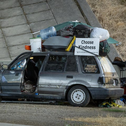 A man rests near a vehicle parked under Interstate