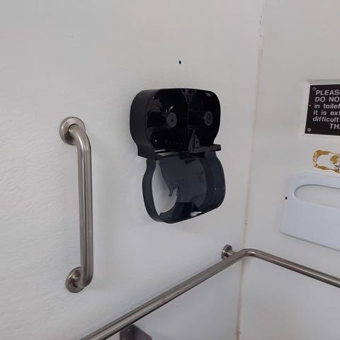 A broken, empty toilet paper dispenser as seen in 