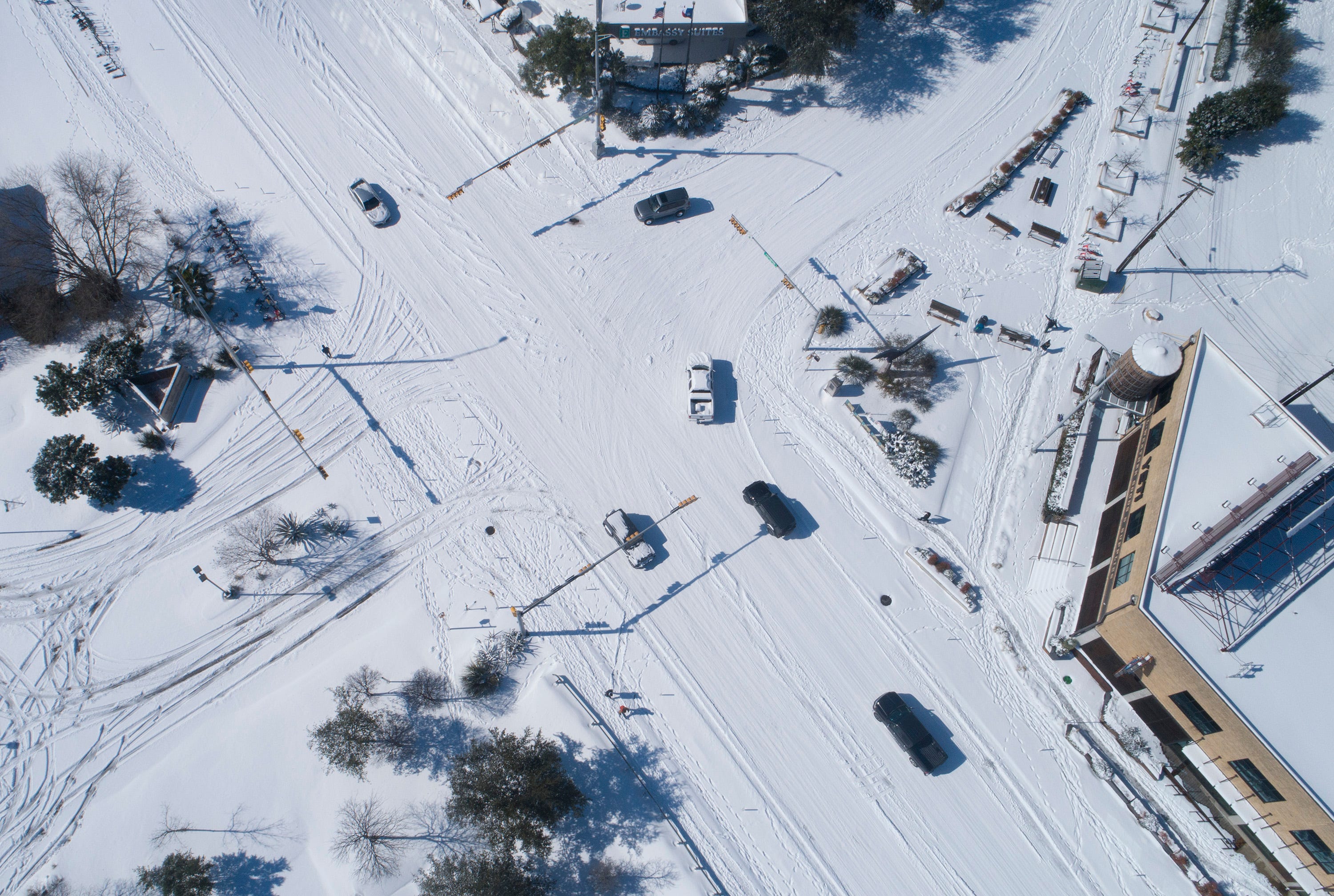 An overhead view of a cars driving through a snowy intersection.