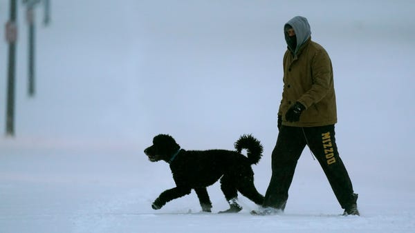 A man walks a dog in fresh snow as temperatures dr