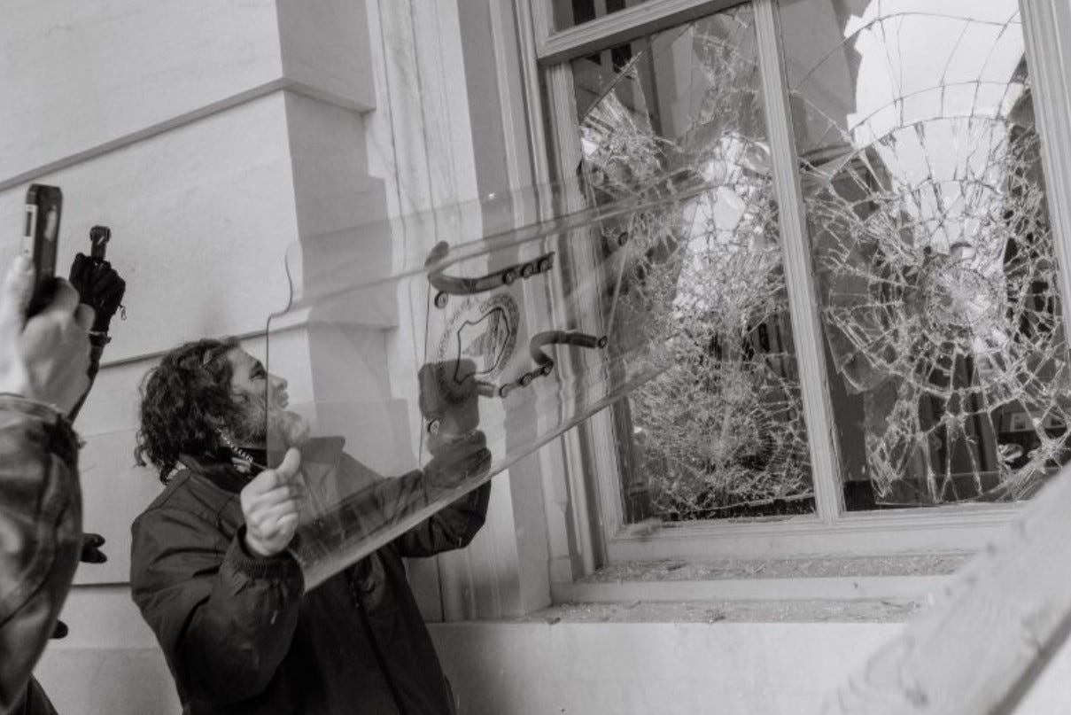 A rioter uses a shield belonging to U.S. Capitol Police to break open a window at the Capitol.