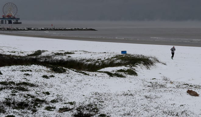 A jogger runs along a snow-covered beach in Galveston, Texas on Monday.