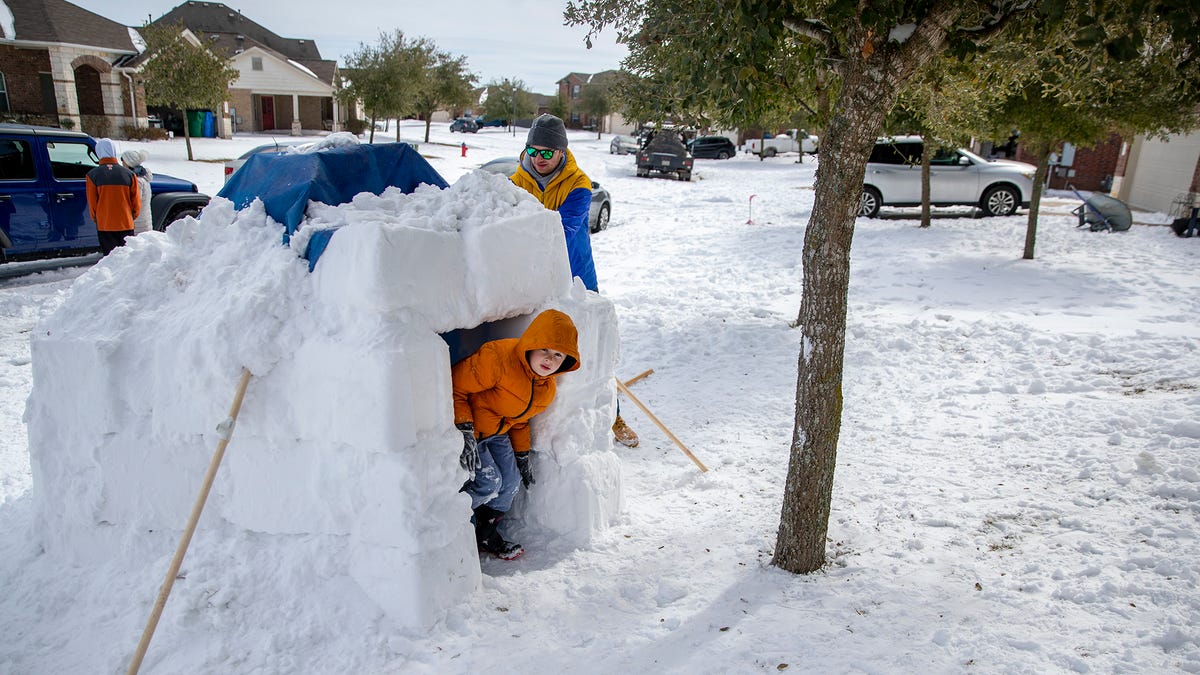 Brett Archibald helps his son build an igloo as his son Avett, 8, peeks out of the igloo in the front yard of their home in Pflugerville, Texas, Tuesday, Feb. 16, 2021. Electricity in the area had been out for about 24 hours.