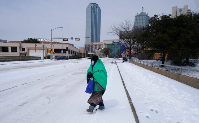 FILE - In this Feb. 16, 2021, file photo, a woman wrapped in a blanket crosses the street near downtown Dallas. As temperatures plunged and snow and ice whipped the state, much of Texas' power grid collapsed, followed by its water systems. Tens of millions huddled in frigid homes that slowly grew colder or fled for safety. (AP Photo/LM Otero, File)