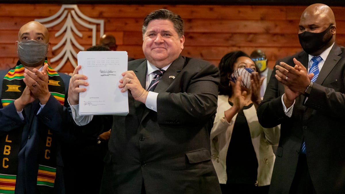Illinois Gov. J.B. Pritzker is joined by lawmakers and community advocates including state Rep. Justin Slaughter, left, and state Sen. Elgie Sims Jr., right, as he signs HB 3653, a sweeping criminal justice and police reform bill, on Monday, Feb. 22, 2021 at Chicago State University. (Brian Cassella/Chicago Tribune via AP)