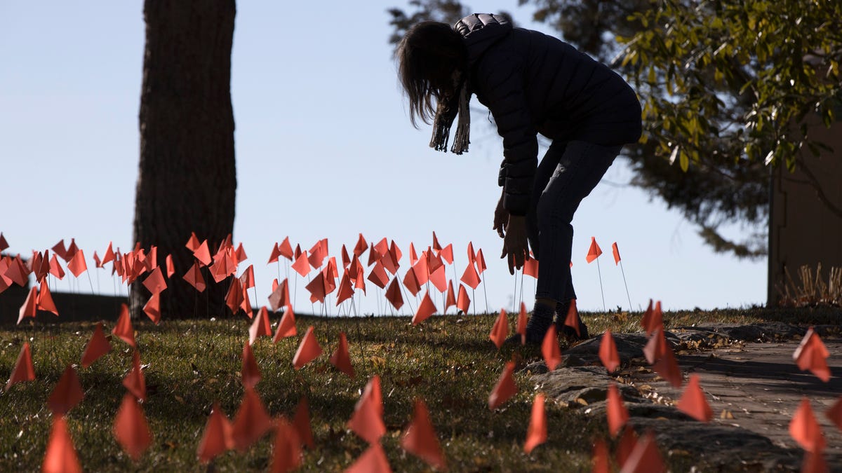 Cindy Pollock does maintenance on the construction flags in her front yard in Boise, Idaho, on Wednesday, Feb. 10, 2021. Pollock began planting the tiny flags across her yard — one for each of the more than 1,800 Idahoans killed by COVID-19 — the toll was mostly a number. Until two women she had never met rang her doorbell in tears, seeking a place to mourn the husband and father they had just lost. 