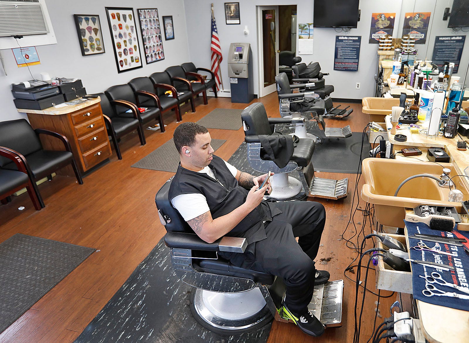 Barber Christian Lavoie owner of Rocco & Sons Barber Shop on Franklin Street Quincy uses his phone on his last day open as Quincy closes most shops other than grocery or pharmacies across the city on Thursday March 19, 2020 Greg Derr/The  Patriot Ledger
