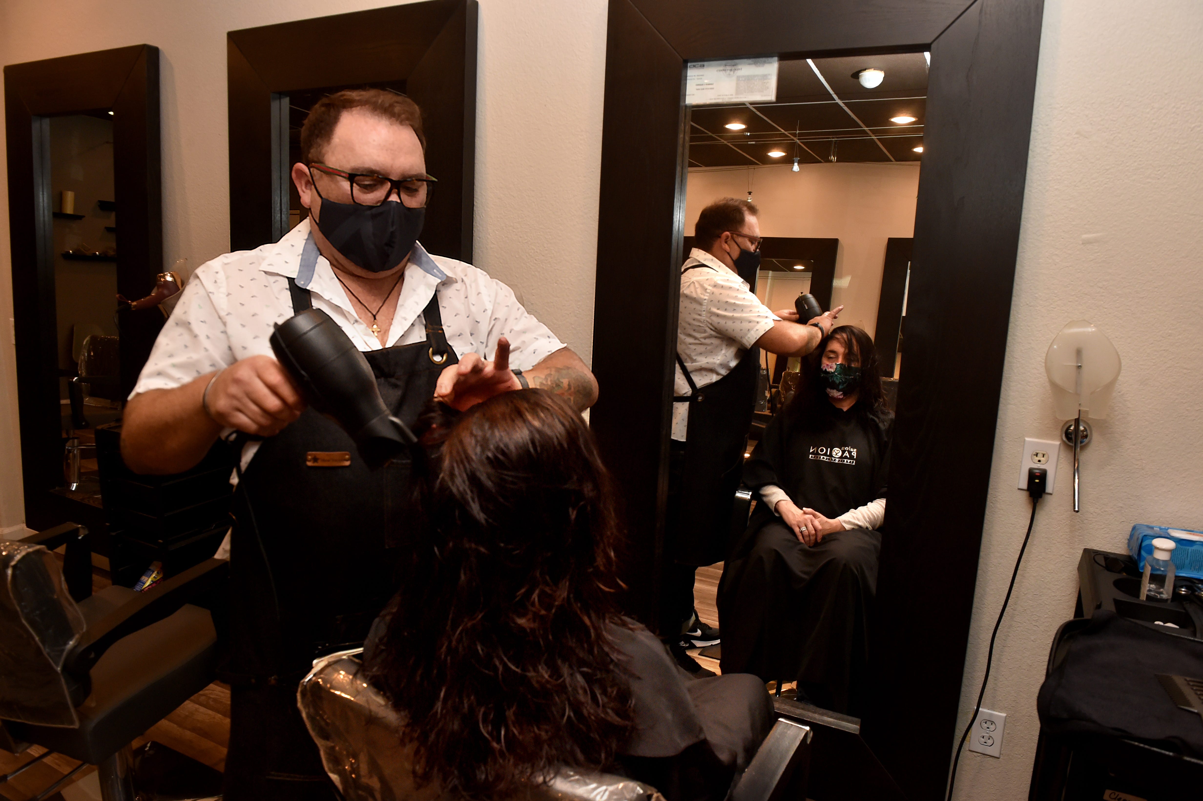 Enrique Ramirez, owner of Salon Passion in Camarillo, styles the hair of Leslie Kaplan on Wednesday, Feb. 24, 2021, as Ramirez and his staff work to keep the business going through the pandemic. After so many ups and downs in 2020, the salon owner nearly closed his business for good but now expects to stay open as more people get vaccinated.