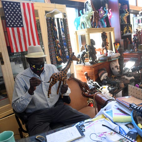Ndiaga Niang, 63, sits at the front counter touching up the paint on a giraffe figurine on Friday, Feb. 26, 2021, at his downtown Fort Pierce store, Africa Art, Antiques and Gifts, in Kraaz Square. Niang, who immigrated to the United States from Senegal more than 30 years ago, imports everything from home decor to clothes, jewelry and accessories from artists across Africa.