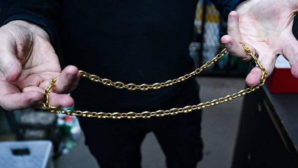 Glenn Sorgenstein holds a gold necklace inside of 
