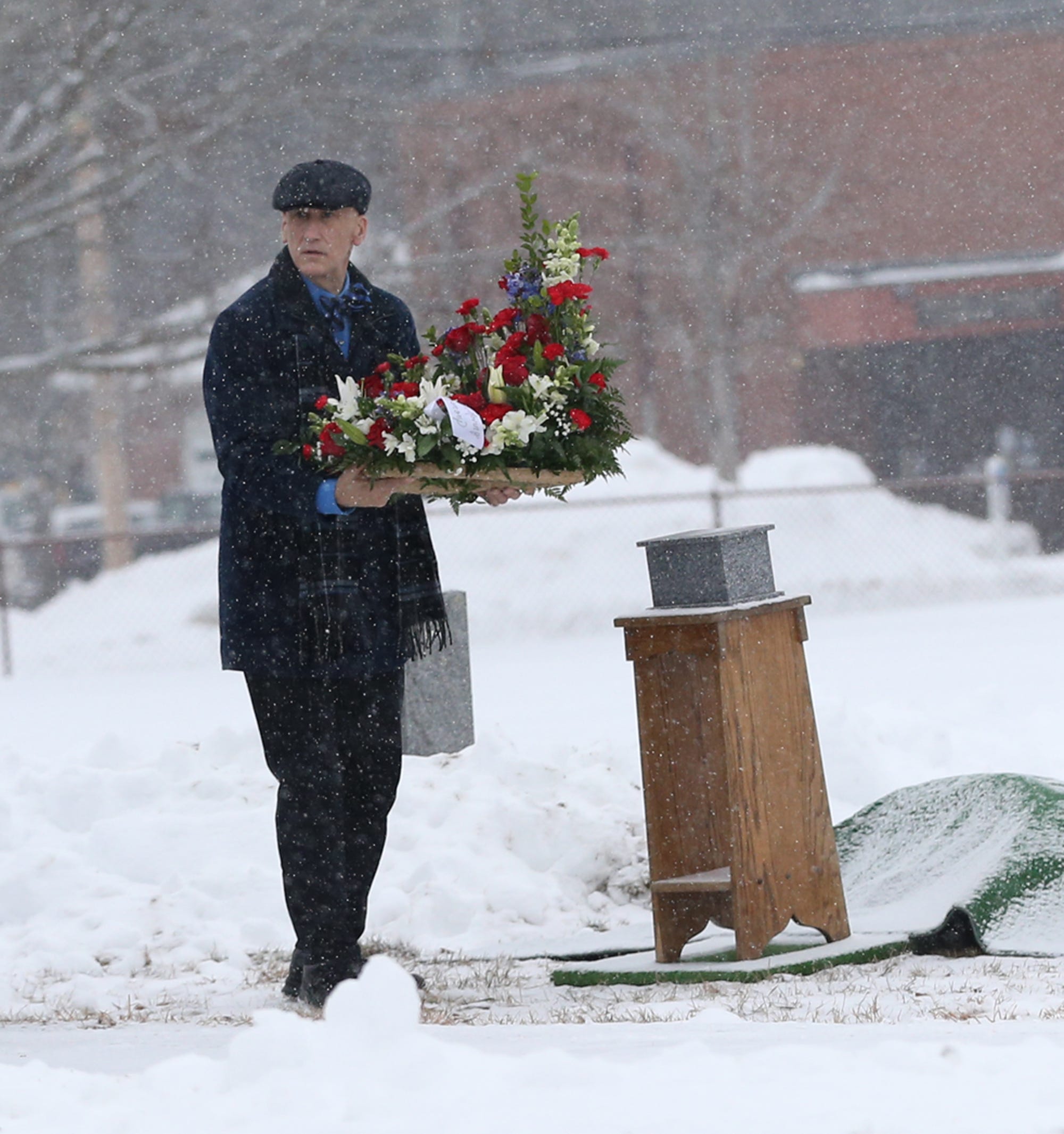 Funeral home director Jeff Pelkey puts a flower arrangement at the base of a podium resting ashes of an elderly gentleman as snow falls gently at Holy Trinity Cemetery in Somersworth, NH.