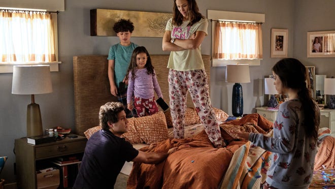 Entire family on the morning of Yes Day. Allison and two of the children stand on the bed, while Carlos kneels next to it and their other daughter stands in front of it.